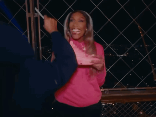 A Woman In A Pink Sweatshirt Holds A Pink Nike Shoe In Her Hand GIF