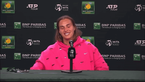 a woman in a pink sweatshirt is sitting in front of a bnp paribas sign