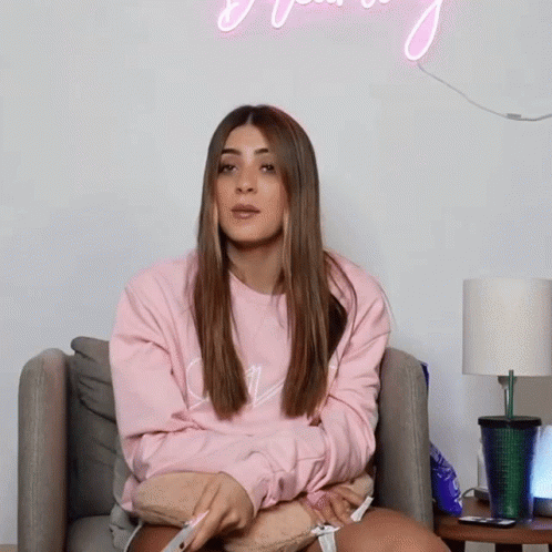 A Woman In A Pink Sweatshirt Sits On A Couch GIF