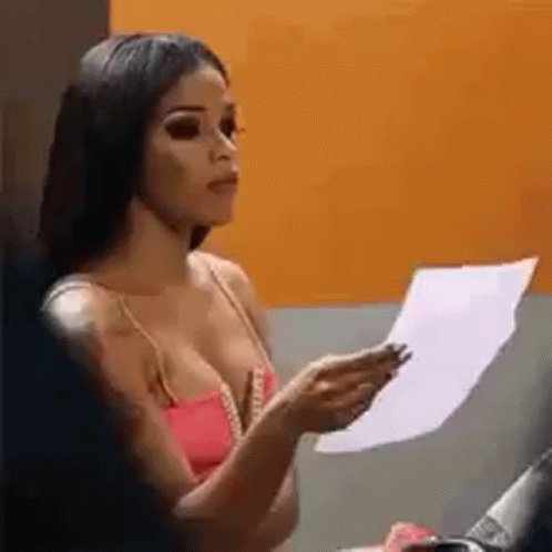 A Woman In A Pink Tank Top Is Holding A Piece Of Paper In Her Hand . GIF