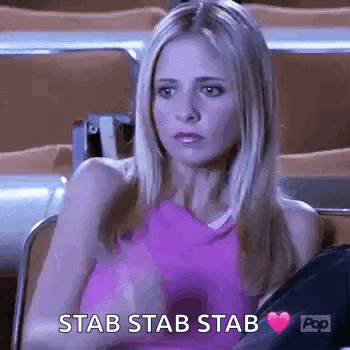 A Woman In A Pink Tank Top Is Sitting In A Stadium With A Heart In Her Hand And The Words `` Stab Stab Stab '' . GIF