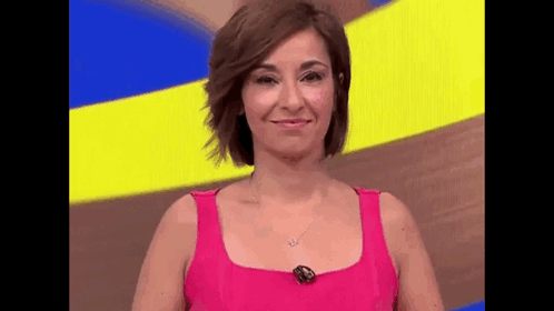 a woman in a pink tank top is smiling while standing in front of a yellow and blue background .