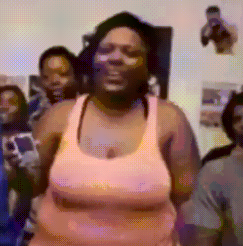 a woman in a pink tank top is standing in front of a group of people and smiling .