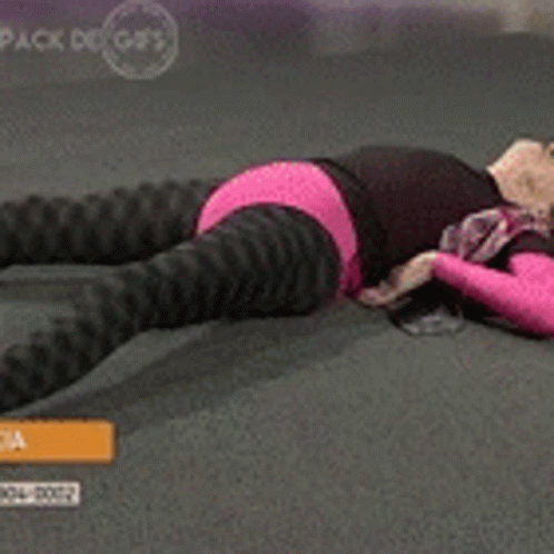 A Woman In A Pink Top And Black Pants Is Laying On The Floor Stretching Her Legs GIF
