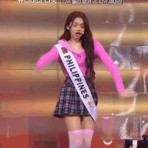 A Woman In A Pink Top And Plaid Skirt Is Wearing A Sash That Says Philippines GIF