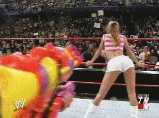 A Woman In A Pink Top And White Shorts Is Dancing In A Wrestling Ring In Front Of A Crowd GIF