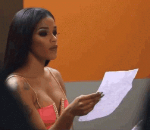 A Woman In A Pink Top Is Holding A Piece Of Paper In Her Hand GIF