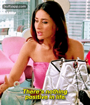 A Woman In A Pink Top Is Sitting At A Table With Handbags And Says `` There 'S Nothing Positive In Life '' . GIF