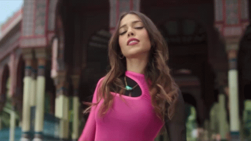 A Woman In A Pink Top Is Standing In Front Of A Building With Her Eyes Closed GIF