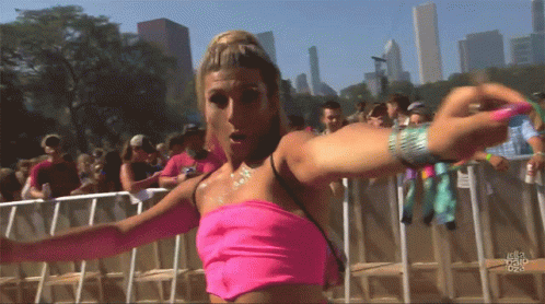 A Woman In A Pink Top Stands In Front Of A Crowd At A Festival GIF