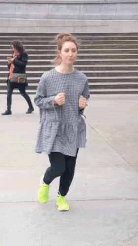A Woman In A Plaid Dress And Neon Yellow Shoes Is Running Down The Street GIF