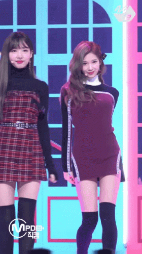 A Woman In A Plaid Dress Is Standing Next To Another Woman In A Black Dress GIF