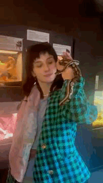 A Woman In A Plaid Jacket Is Holding A Snake Over Her Head . GIF