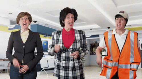 A Woman In A Plaid Jacket Stands Next To Two Other Women GIF