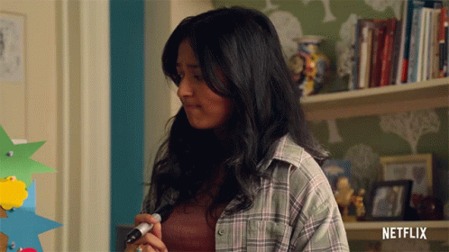 A Woman In A Plaid Shirt Is Holding A Marker In Front Of A Shelf With Netflix Written On It GIF