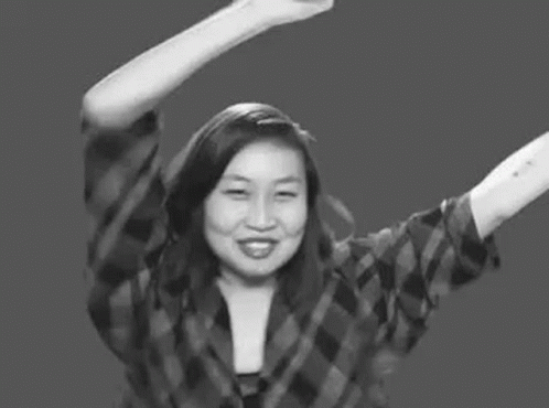 A Woman In A Plaid Shirt Is Raising Her Arms In The Air . GIF