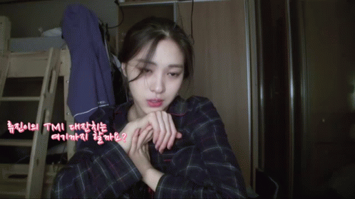 A Woman In A Plaid Shirt Is Sitting In A Room With Korean Writing On The Walls GIF