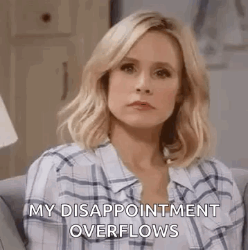 A Woman In A Plaid Shirt Is Sitting On A Couch And Making A Sad Face . GIF