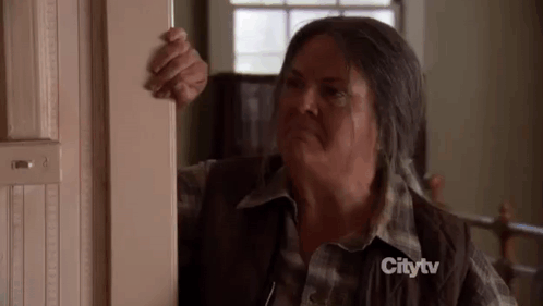A Woman In A Plaid Shirt Is Standing In A Doorway And Looking Out . GIF