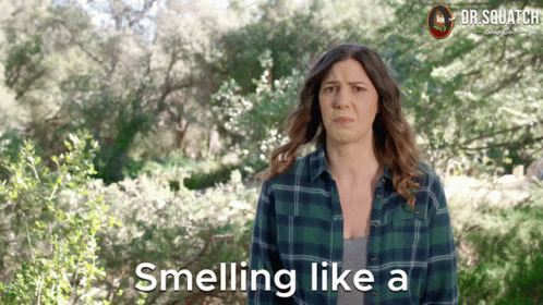 A Woman In A Plaid Shirt Is Standing In The Woods And Says Smelling Like A GIF