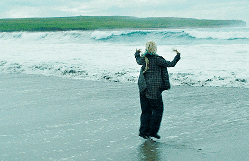 A Woman In A Plaid Shirt Is Standing On A Beach GIF