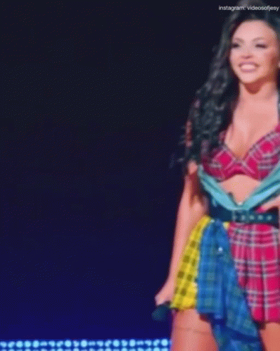 A Woman In A Plaid Top And Skirt Is Standing On A Stage . GIF