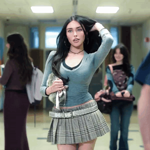 A Woman In A Pleated Skirt Holds Her Hair In A Hallway GIF