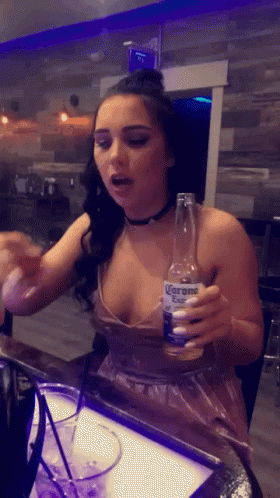 A Woman In A Plunging Neckline Holds A Bottle Of Corona GIF