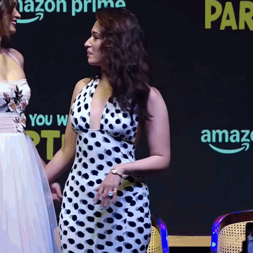 A Woman In A Polka Dot Dress Stands Next To Another Woman In A White Dress GIF