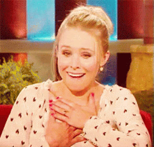 A Woman In A Polka Dot Shirt Is Smiling With Her Hand On Her Chest GIF