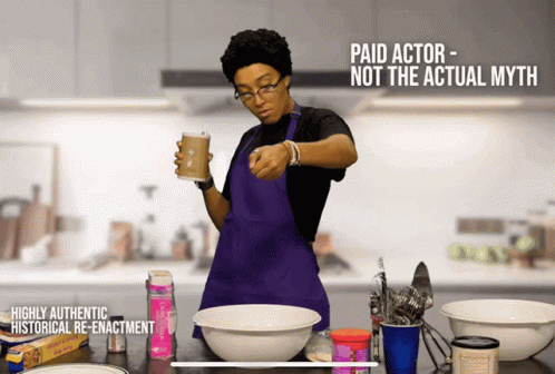 A Woman In A Purple Apron Is Holding A Cup Of Coffee In A Kitchen GIF