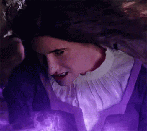 A Woman In A Purple Dress And A White Collar Is Standing In Front Of A Purple Light . GIF