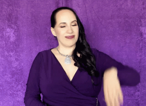 A Woman In A Purple Dress Is Dancing In Front Of A Purple Wall . GIF