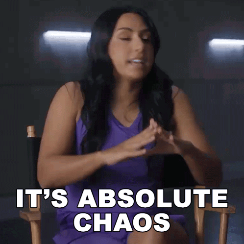 A Woman In A Purple Dress Is Sitting In A Director 'S Chair And Saying It 'S Absolute Chaos GIF