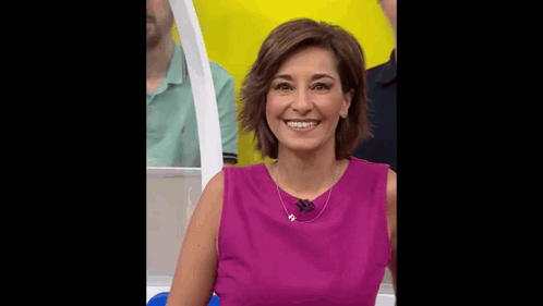 a woman in a purple dress is smiling in front of a yellow wall .