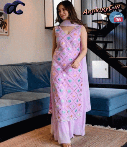 A Woman In A Purple Dress Is Standing In Front Of A Blue Couch GIF