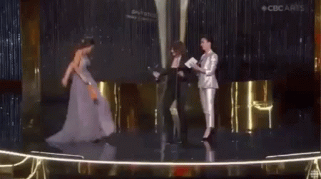 A Woman In A Purple Dress Is Standing On A Stage Holding A Trophy . GIF