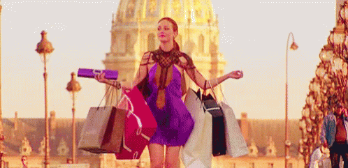 A Woman In A Purple Dress Is Walking Down A Street Holding Shopping Bags . GIF