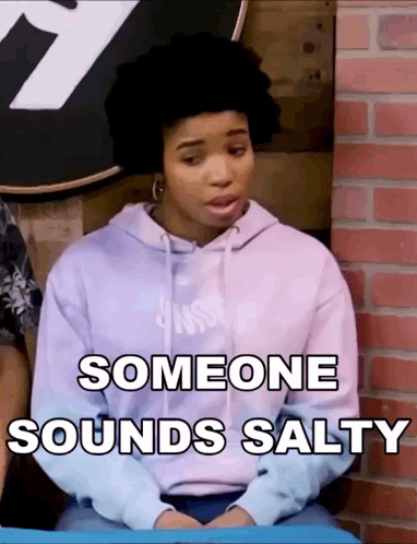 A Woman In A Purple Hoodie Is Sitting In Front Of A Brick Wall And Someone Sounds Salty GIF