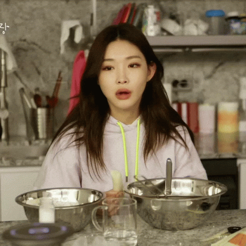 A Woman In A Purple Hoodie Sits At A Counter With Bowls Of Food And A Glass Of Water GIF