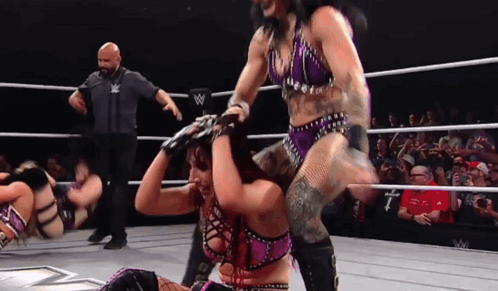 A Woman In A Purple Outfit Is Being Lifted By A Man In A Wrestling Ring GIF