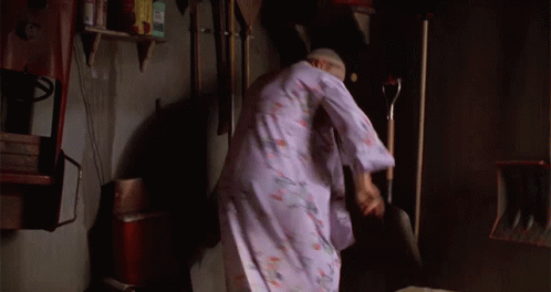 A Woman In A Purple Robe Is Standing In A Room With A Shovel GIF