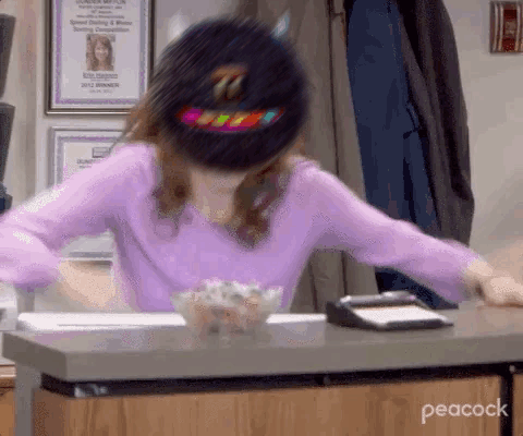 A Woman In A Purple Shirt And A Black Hat Is Sitting At A Desk . GIF