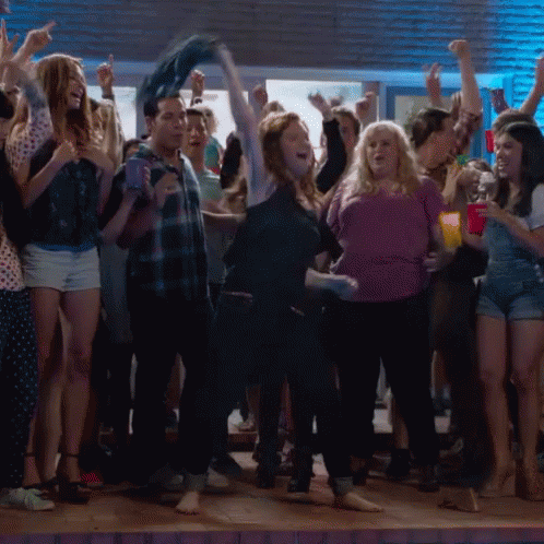 A Woman In A Purple Shirt Is Dancing In A Crowd Of People GIF
