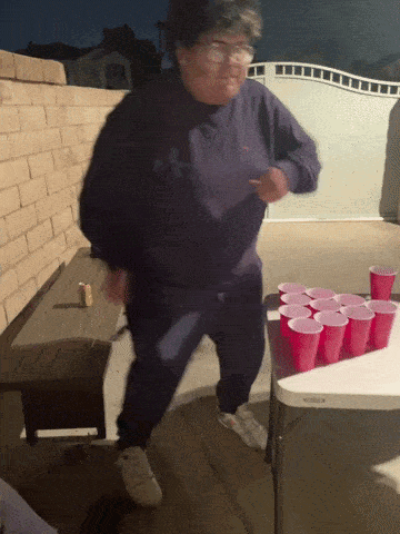 A Woman In A Purple Shirt Is Dancing In Front Of A Table Full Of Red Cups GIF