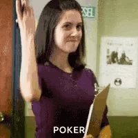 A Woman In A Purple Shirt Is Holding A Clipboard And Waving At The Camera . GIF
