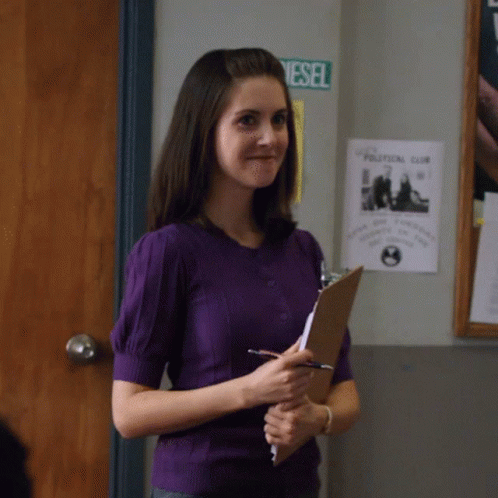 A Woman In A Purple Shirt Is Holding A Clipboard In Front Of A Political Club Poster GIF