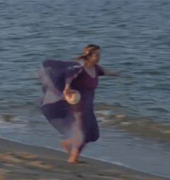 A Woman In A Purple Shirt Is Running Into The Ocean GIF