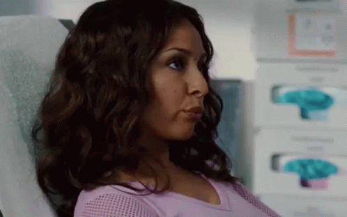 A Woman In A Purple Shirt Is Sitting In A Hospital Bed . GIF
