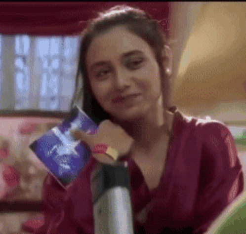 A Woman In A Purple Shirt Is Smiling While Holding A Book . GIF